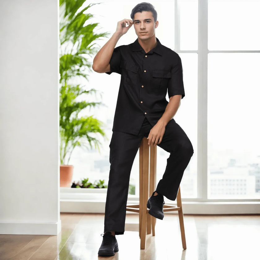 Man wearing modern black short-sleeve shirt and pants, seated indoors with city view.