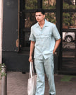 Man wearing light blue linen shirt and pants set, holding a tote bag outdoors