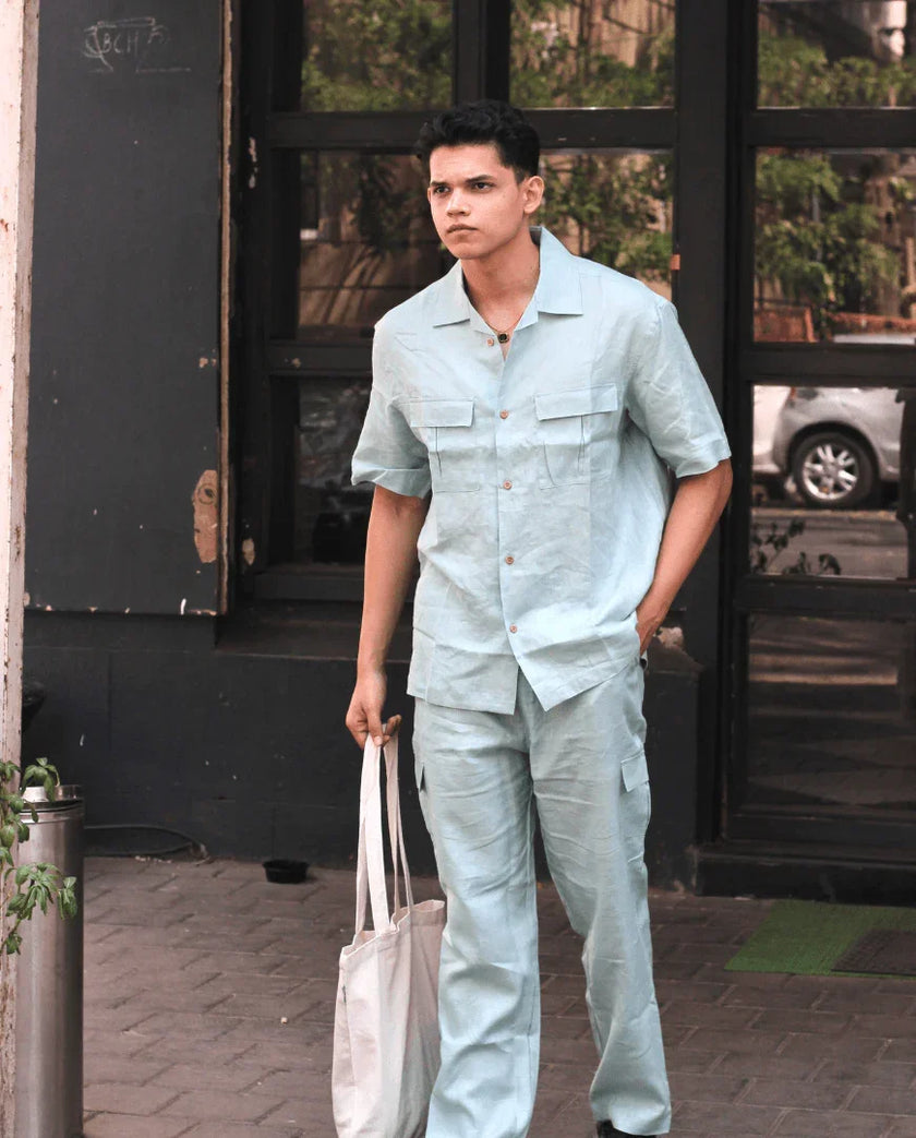 Man wearing light blue linen shirt and pants set, holding a tote bag outdoors