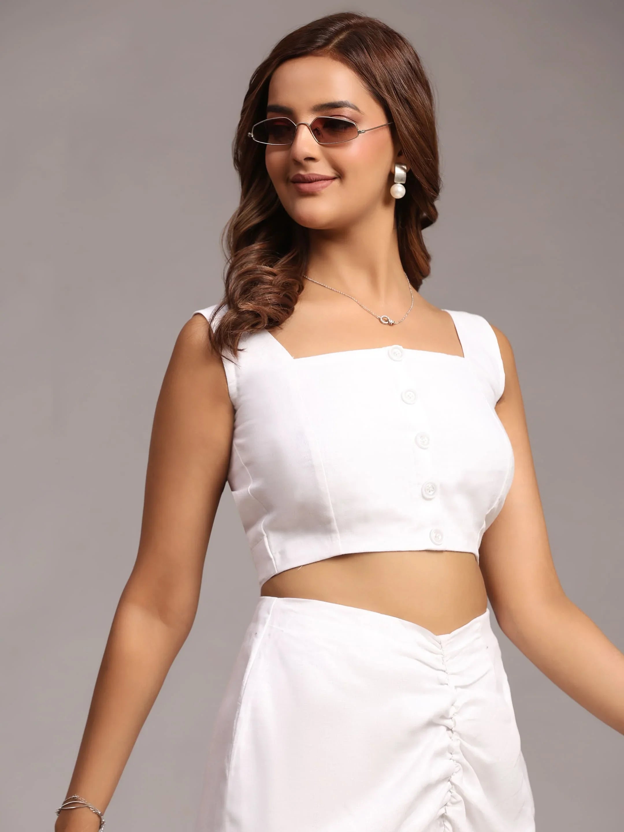 Woman in white crop top and high-waisted skirt, wearing sunglasses and pearl earrings