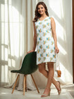 Woman in a sleeveless white printed dress with sandals, posing indoors by a green chair