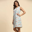 Woman wearing a sleeveless white dress with playful colorful prints, posing indoors