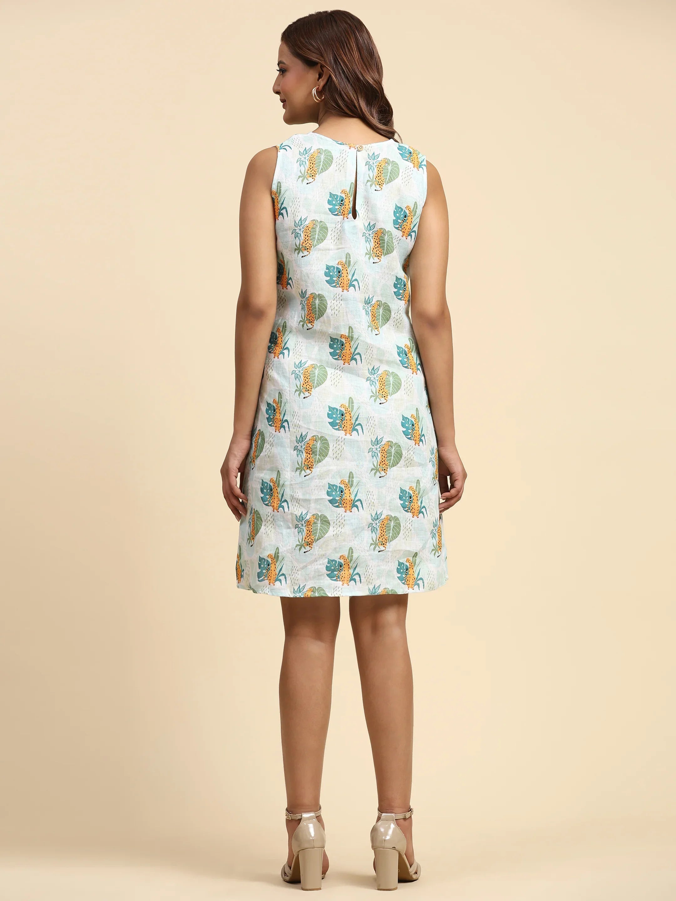 Woman in sleeveless printed dress with leaf pattern, standing on beige background