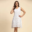 Woman wearing a sleeveless white dress with subtle floral print, posing against beige background