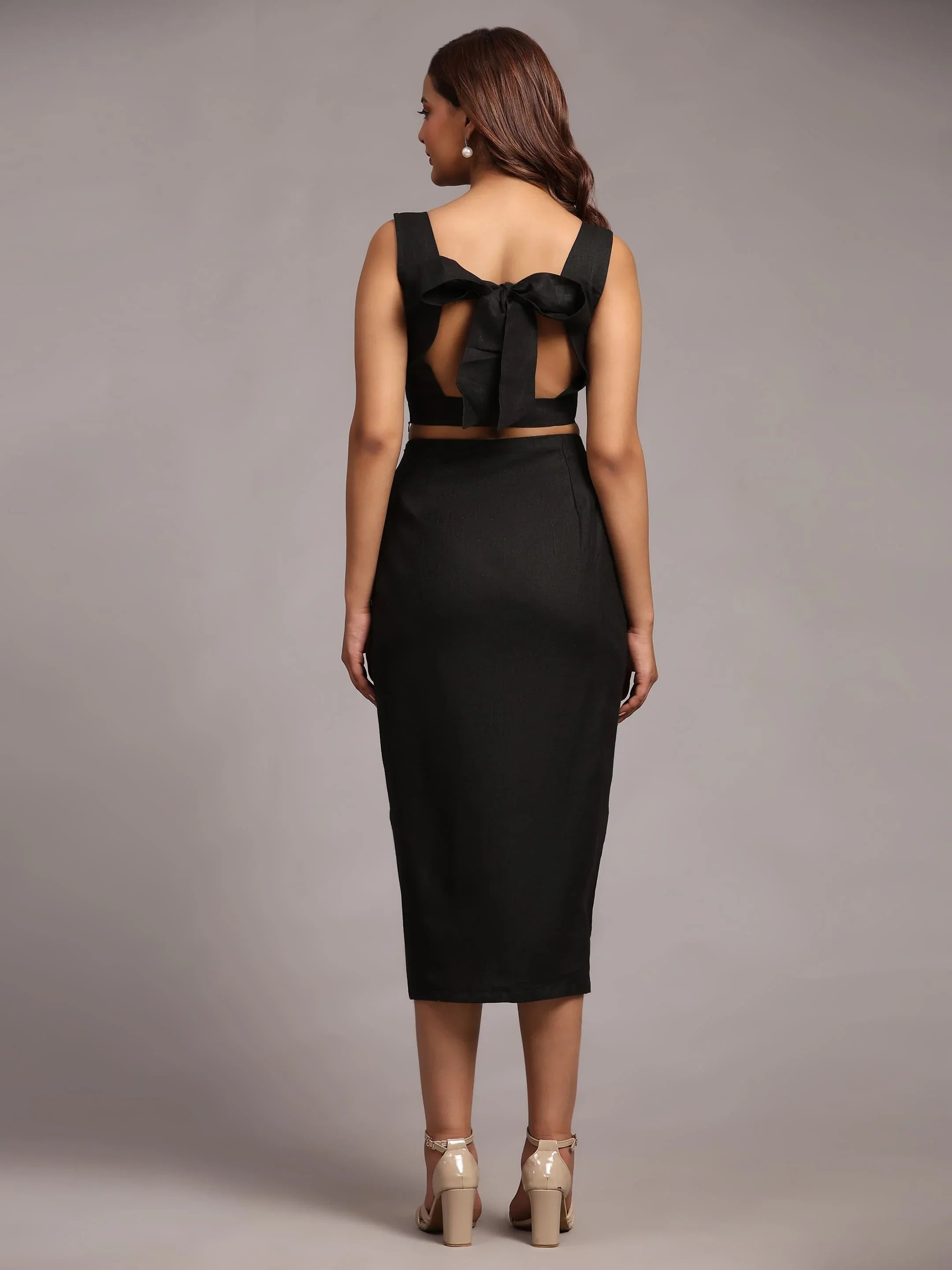 Woman in black sleeveless midi dress with open back and large bow detail, studio setting