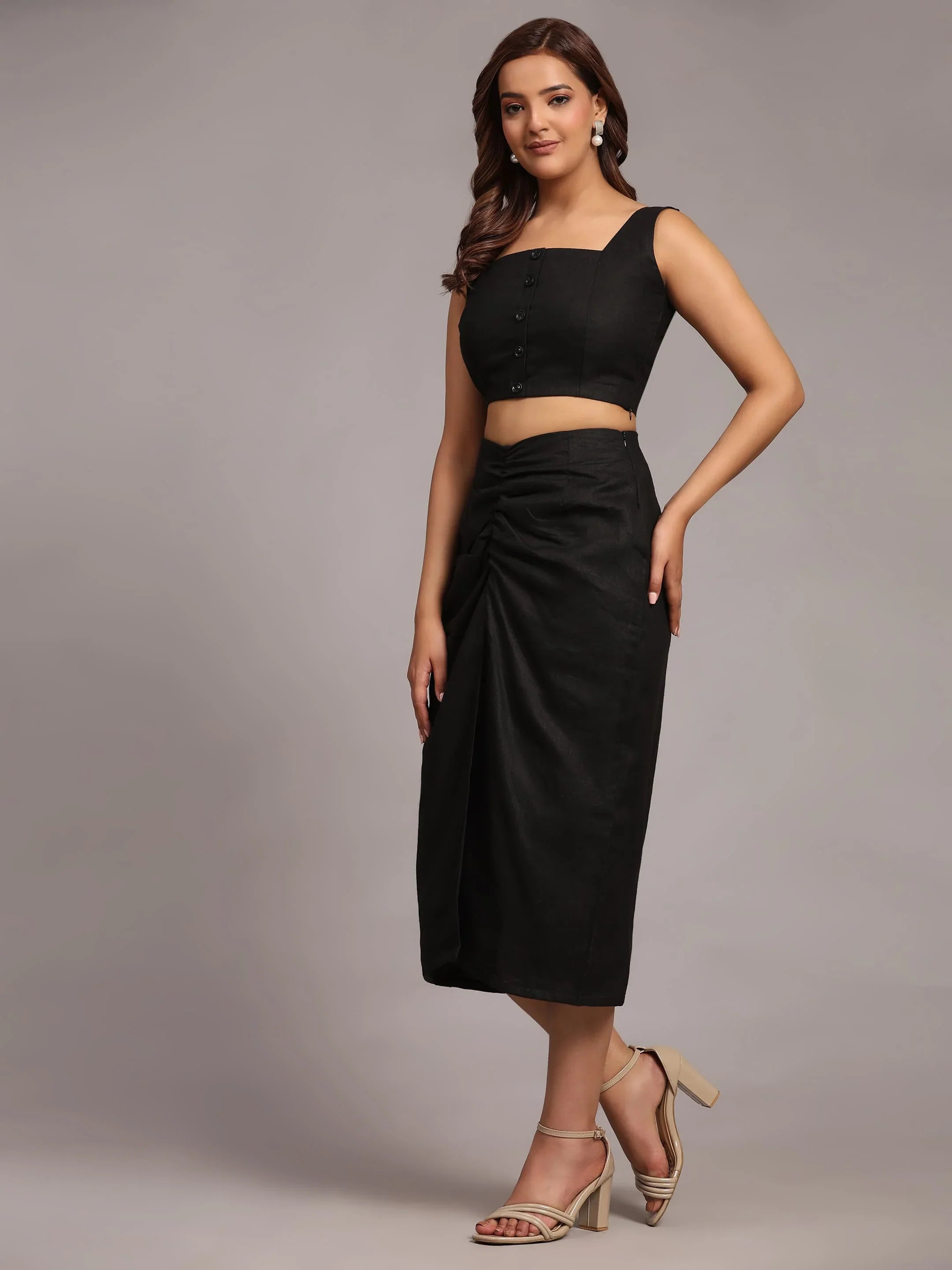 Woman in black sleeveless crop top and ruched midi skirt, posing in neutral studio