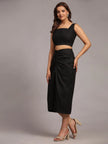 Woman in black sleeveless crop top and ruched midi skirt, posing in neutral studio
