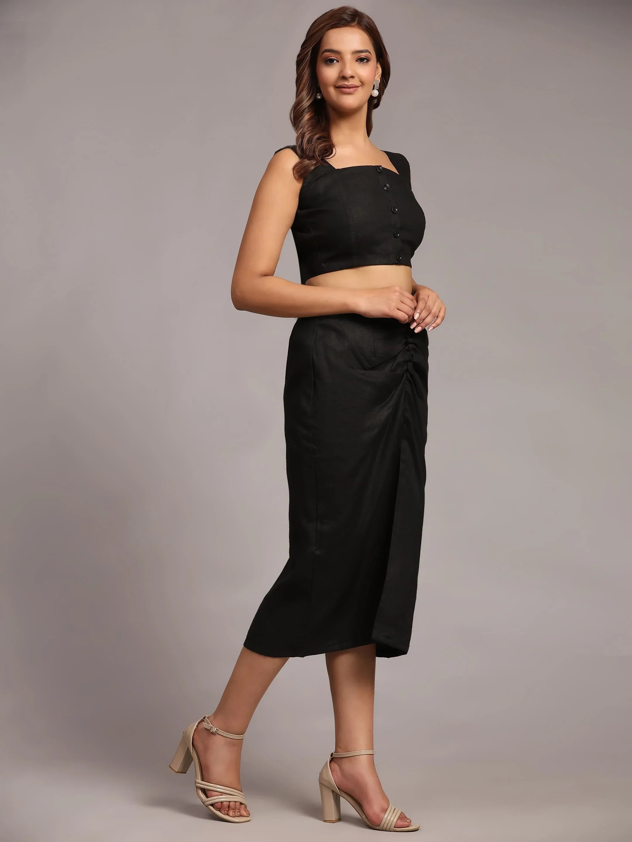Woman wearing a black sleeveless crop top and matching high-waisted skirt with heels