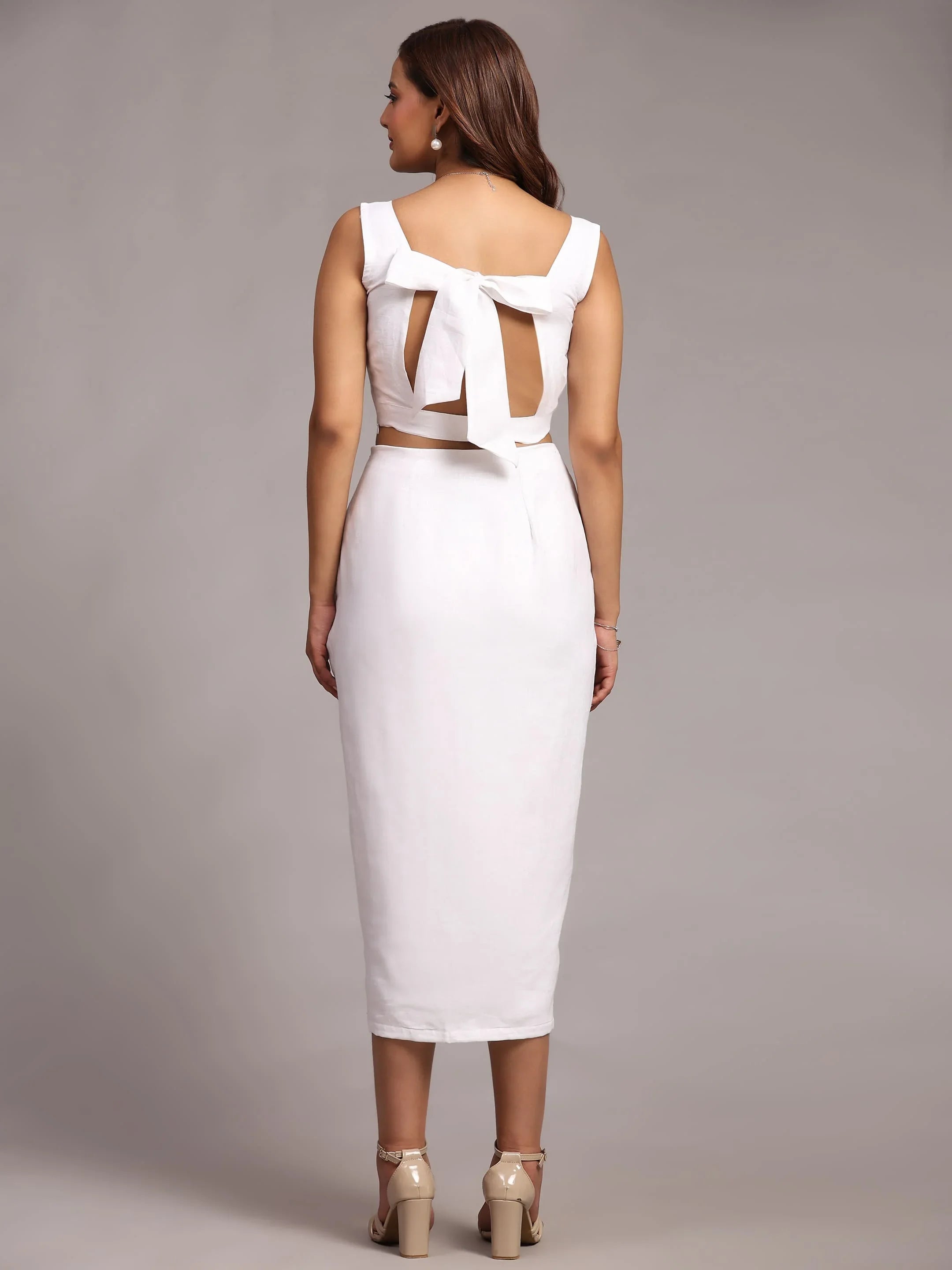 Woman wearing a white midi dress with back bow detail and block heels, studio background