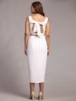 Woman wearing a white midi dress with back bow detail and block heels, studio background