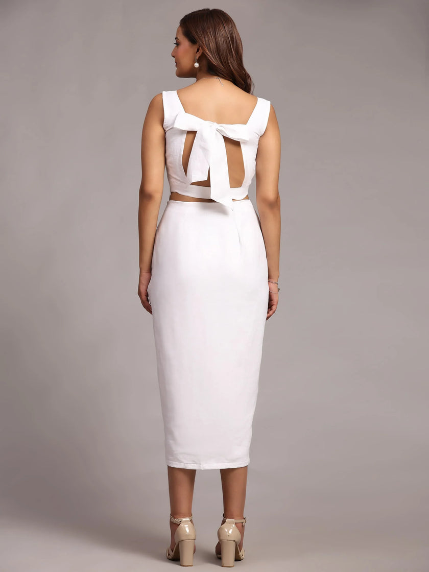 Woman wearing a white midi dress with back bow detail and block heels, studio background