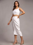 Woman in a white sleeveless crop top and midi skirt with front slit, wearing heels