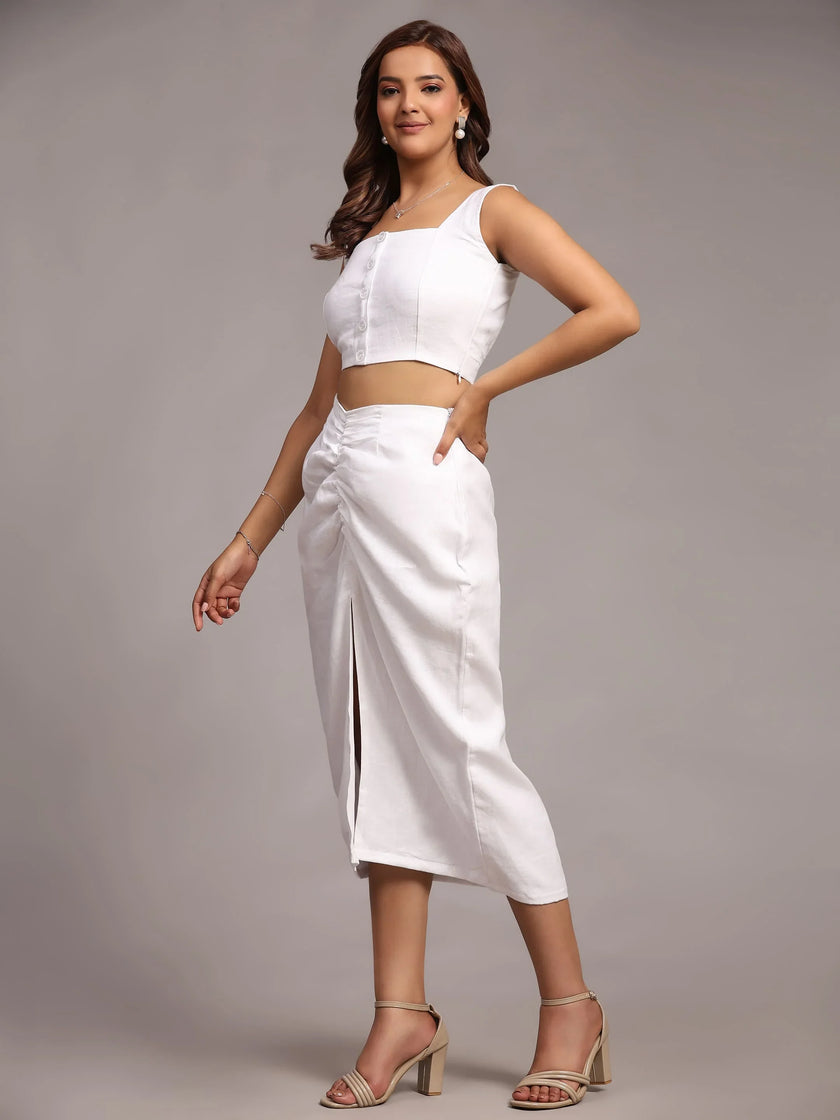 Woman in a white sleeveless crop top and midi skirt with front slit, wearing heels
