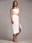 Woman in a white sleeveless crop top and matching high-waisted skirt with side slit