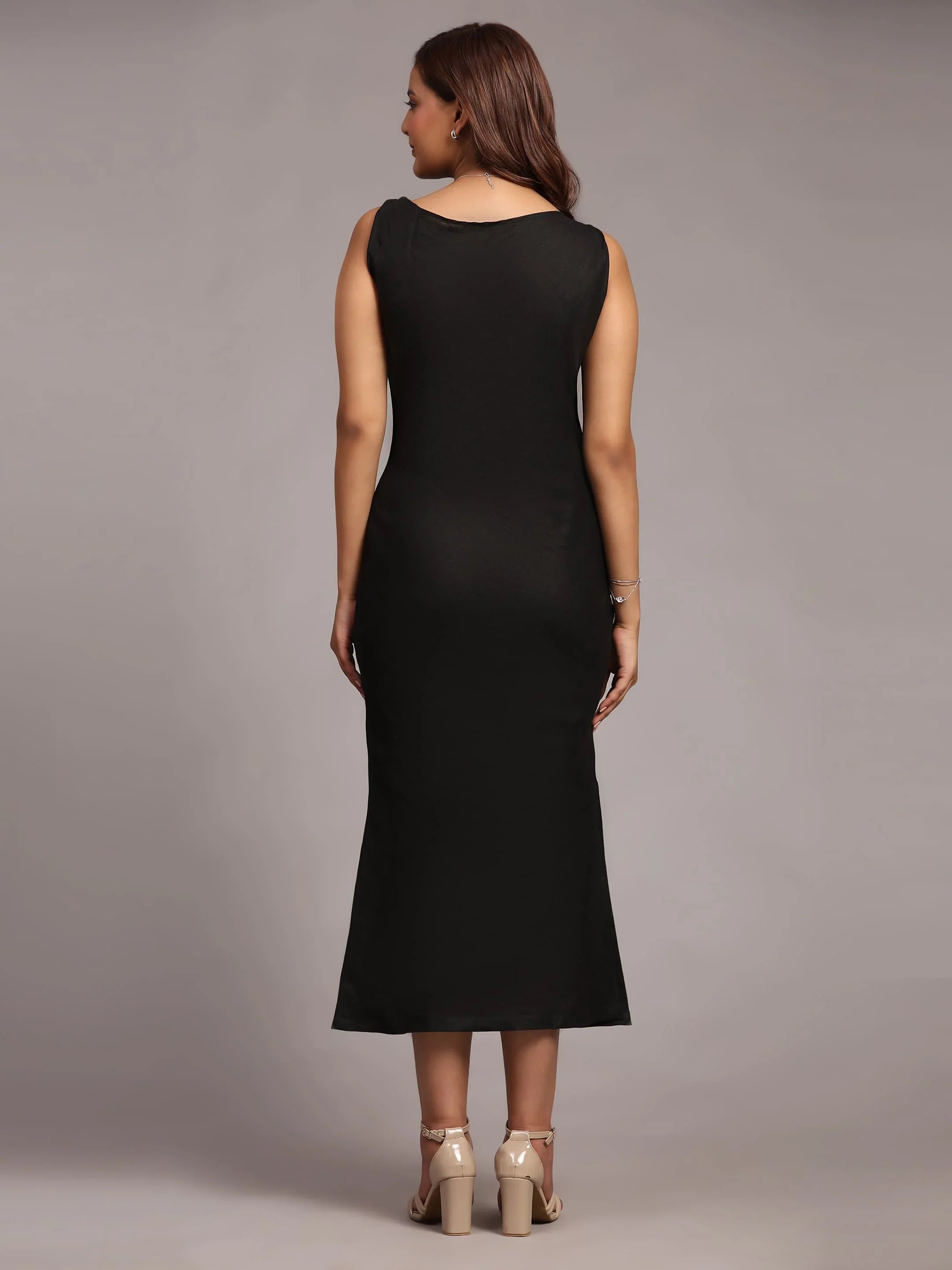 Woman in sleeveless black midi dress and beige heels, shown from the back, studio setting