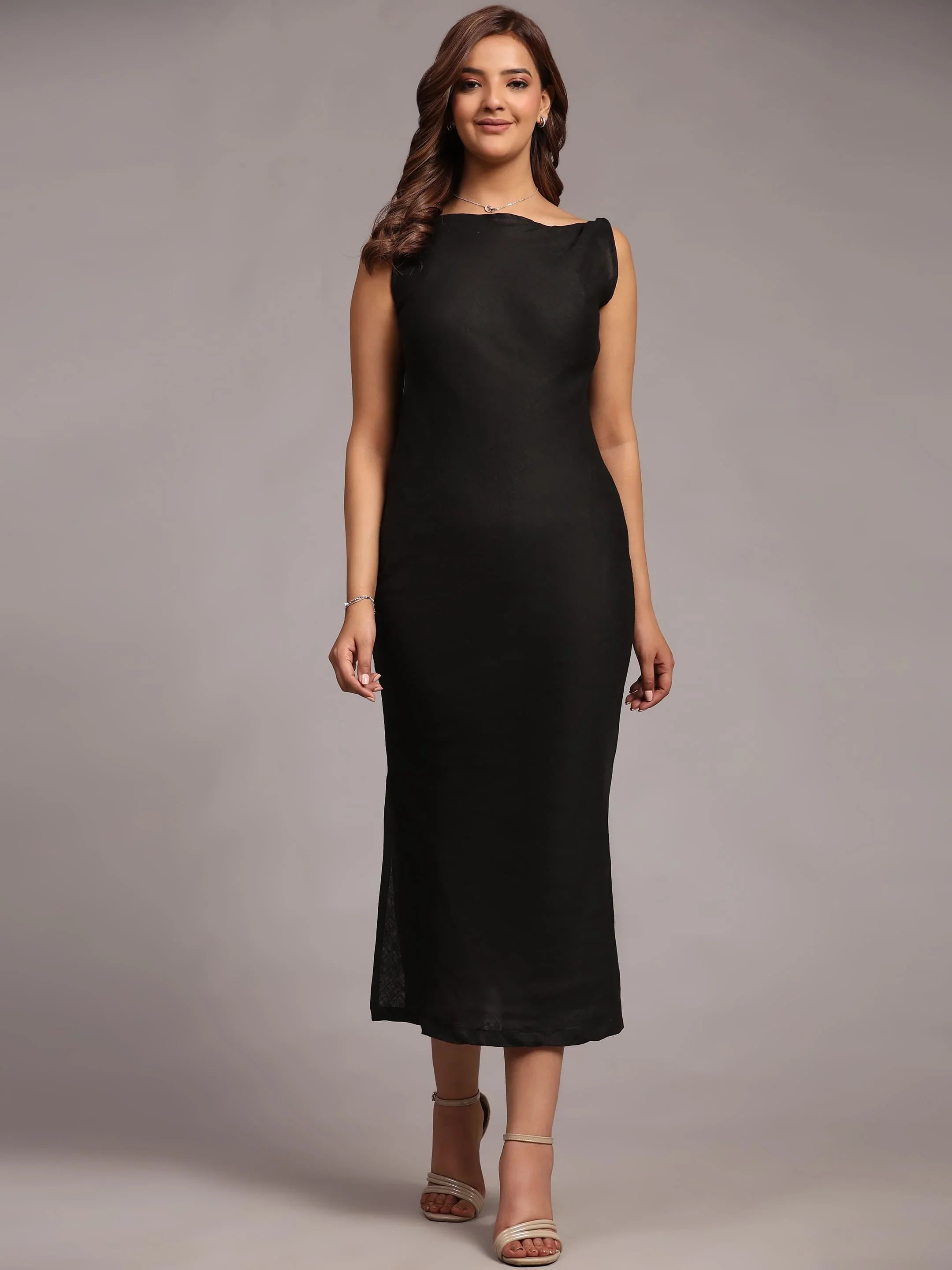 Woman in sleeveless black midi dress and heels posing against a neutral background