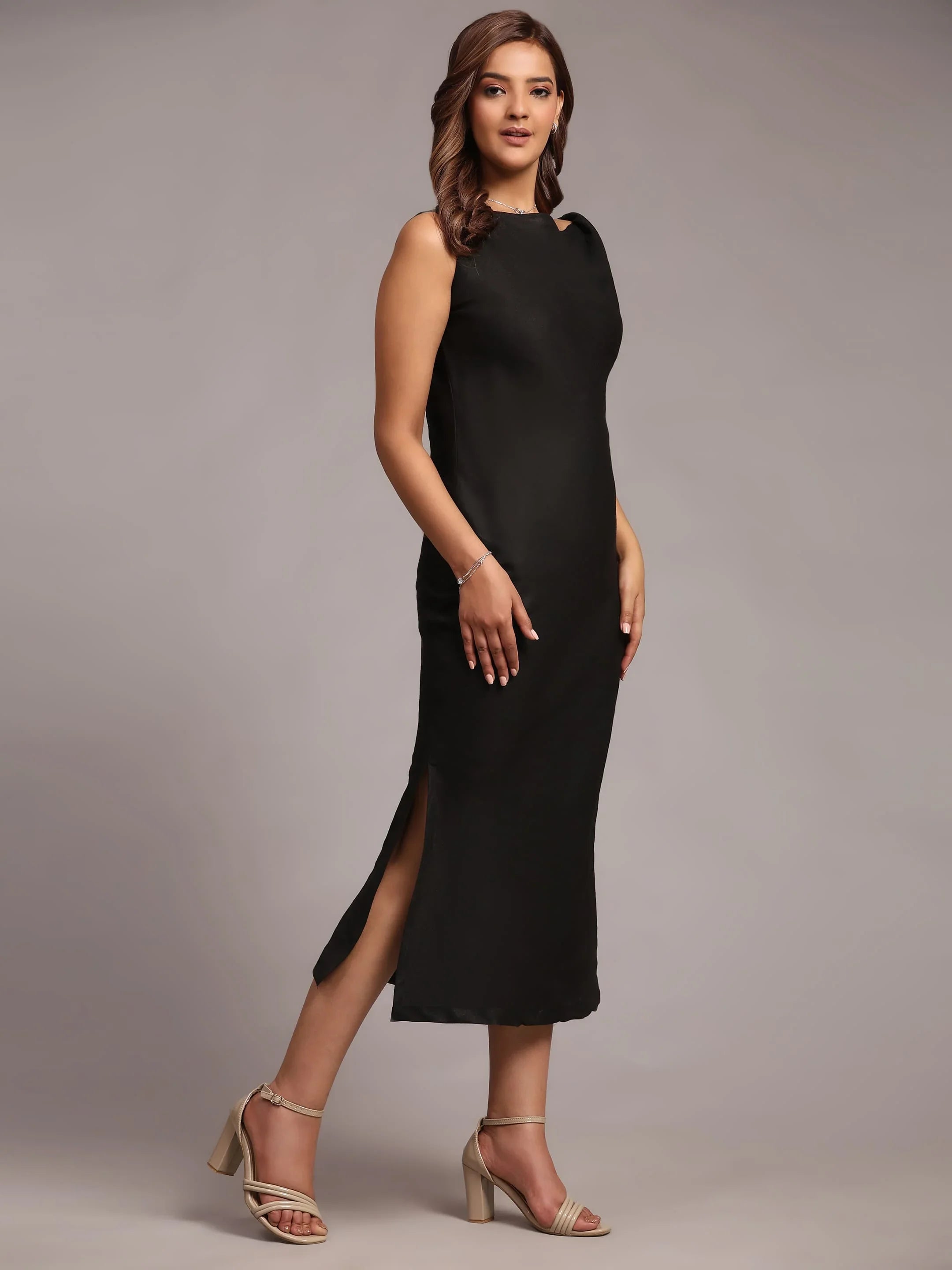 Woman in a sleeveless black midi dress with side slit and nude block heel sandals