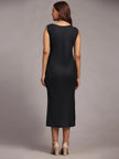 Woman in sleeveless black midi dress and heels, back view, in studio setting