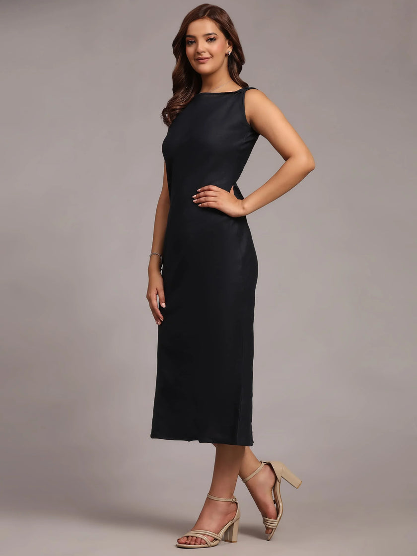 Woman in sleeveless black midi dress and nude heels poses against plain studio background