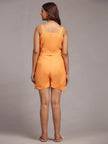 Woman wearing an orange sleeveless top and matching shorts, back view, studio setting