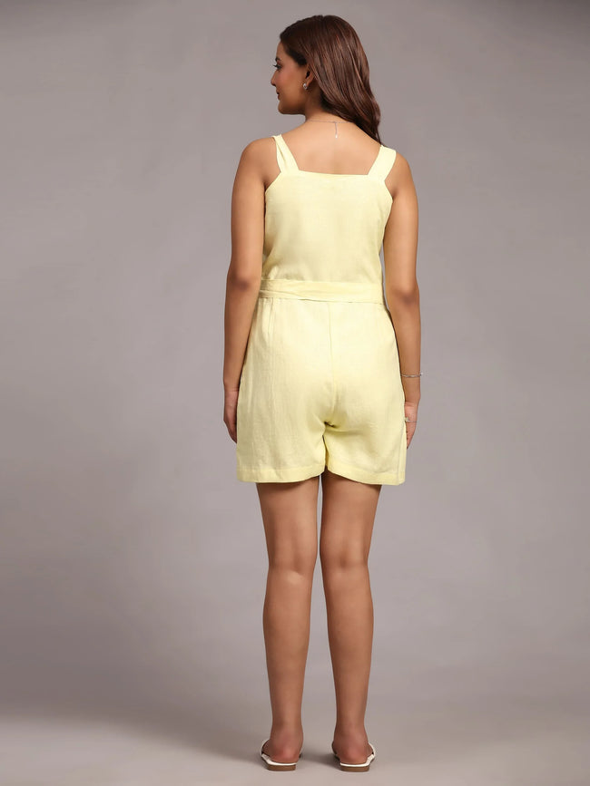 Woman in a pale yellow sleeveless romper, back view, minimal studio background