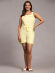 Woman wearing a light yellow sleeveless playsuit with waist tie and white sandals