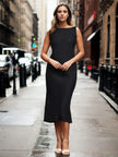 Woman in a sleeveless black midi dress and heels standing on a city street