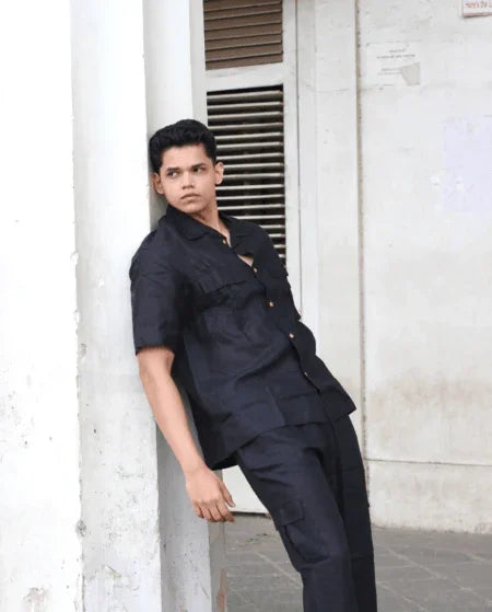 Man in black button-up shirt and trousers posing outdoors against white column