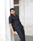 Man in black button-up shirt and trousers posing outdoors against white column