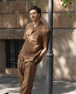 Man wearing brown linen shirt and pants set, standing outdoors by a wall and lamppost
