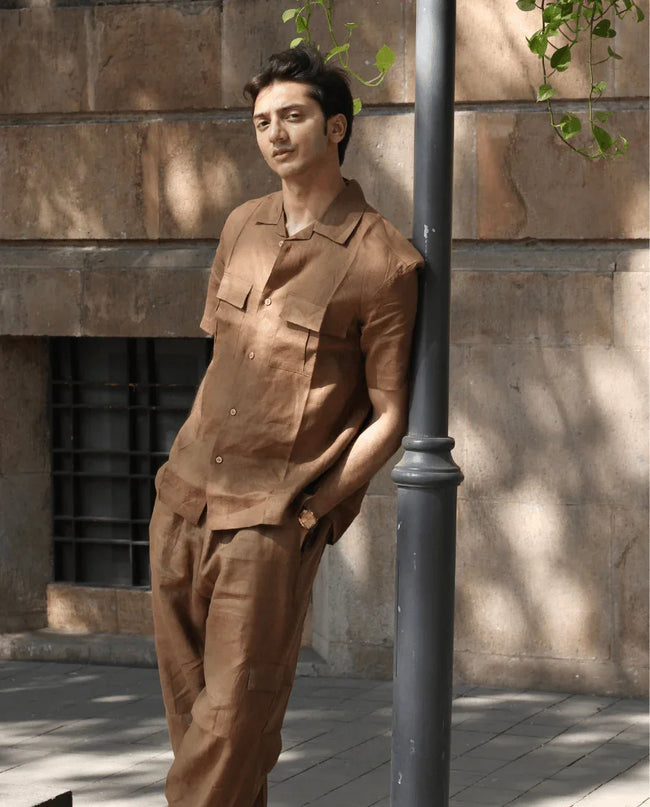 Man wearing brown linen shirt and pants set, standing outdoors by a wall and lamppost