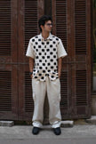 Man wearing checkerboard short sleeve shirt and cream cargo pants, standing outside