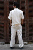 Man in cream short-sleeve shirt and pants set, standing outdoors facing wooden shutters