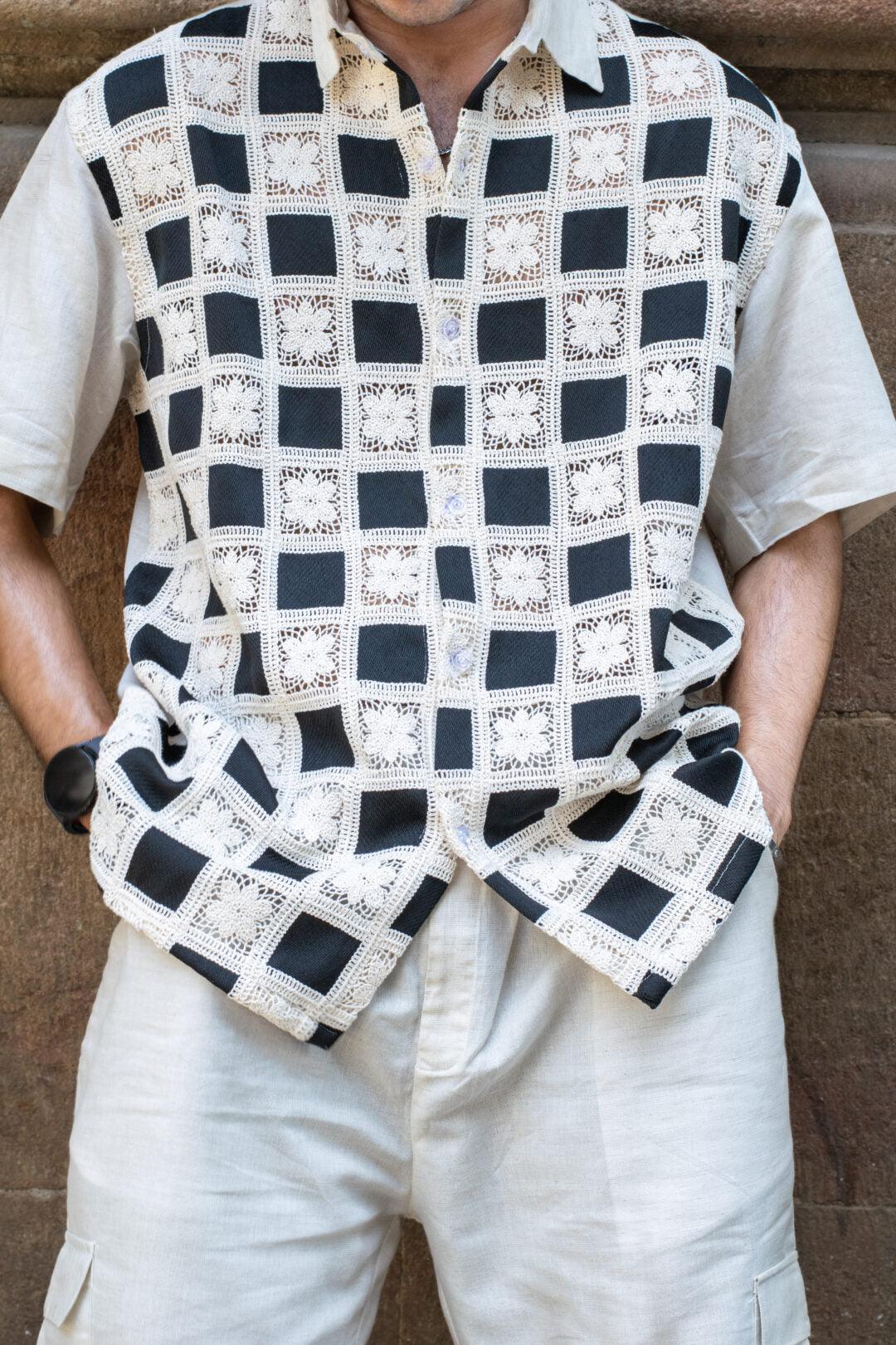 Man wearing a short-sleeve shirt with black and cream crochet square pattern and cream shorts