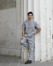 Man in modern light grey shirt and matching pants, leaning against white columns outdoors