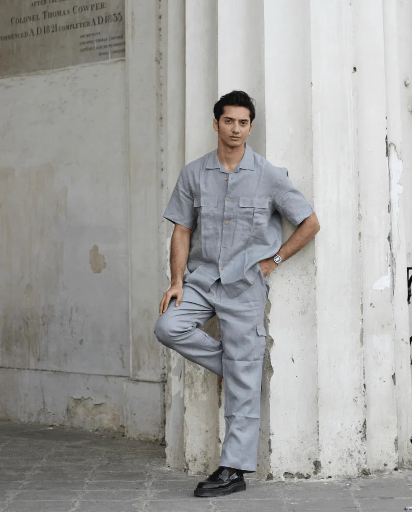 Man in modern light grey shirt and matching pants, leaning against white columns outdoors