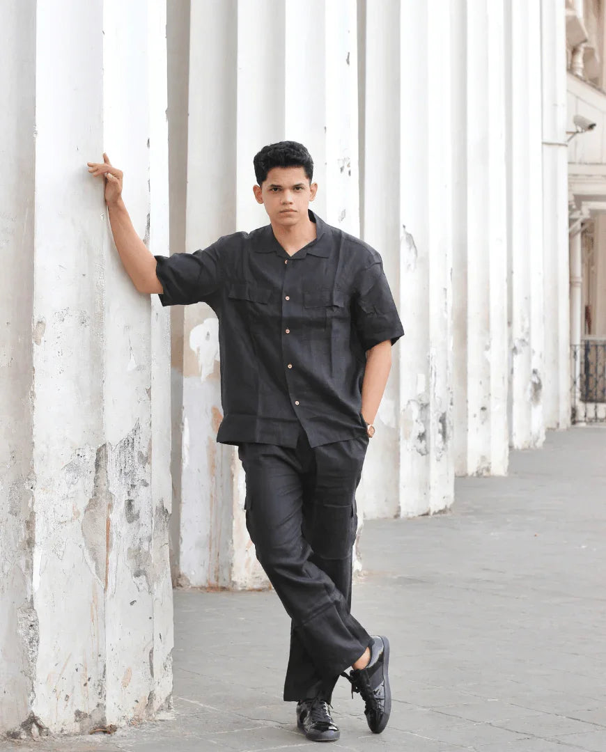 Man in black button-up shirt and trousers posing by white columns outdoors