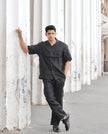 Man in black button-up shirt and trousers posing by white columns outdoors