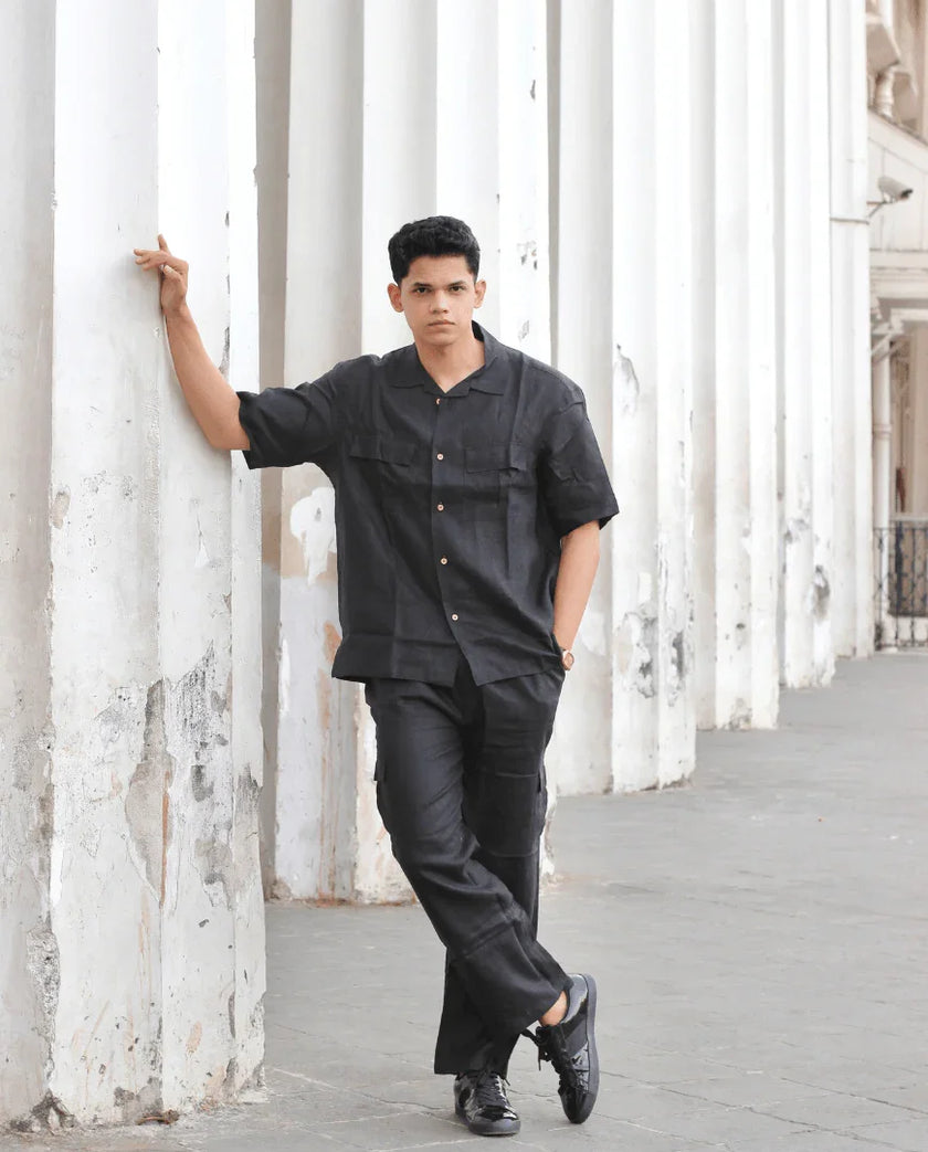 Man in black button-up shirt and trousers posing by white columns outdoors