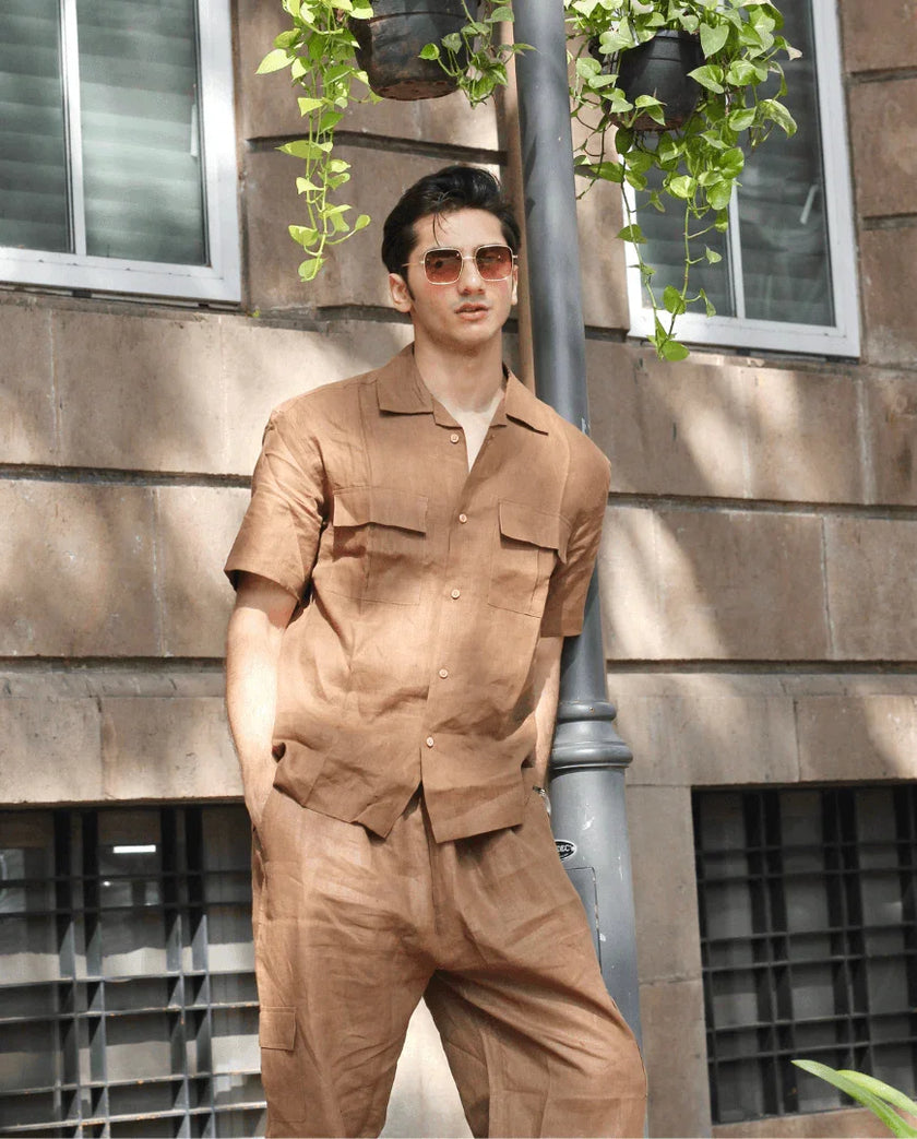 Man wearing a brown short sleeve button-up shirt and matching pants, posing outdoors.