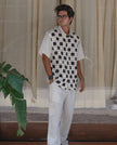 Man wearing black and white checkered short sleeve shirt and white cargo pants, standing indoors.
